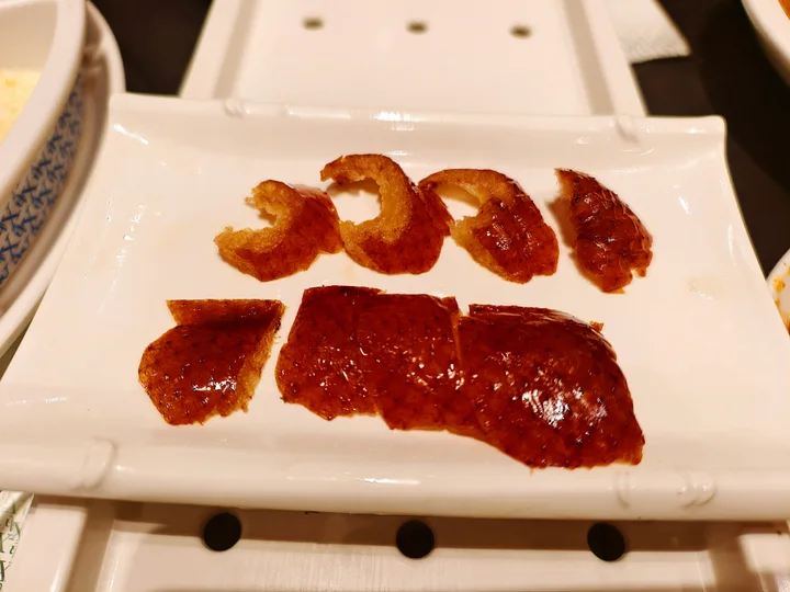 Skin-forward pieces of Beijing roast duck arranged on a white plate before the meatier slices