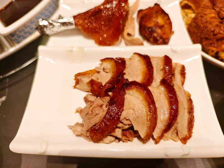 Slices of Beijing roast duck with crisp skin, a thin fat layer and tender meat on a white plate