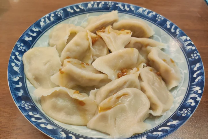 An original photograph of boiled northeastern dumplings served on a blue-and-white plate with a little seasoning on the surface