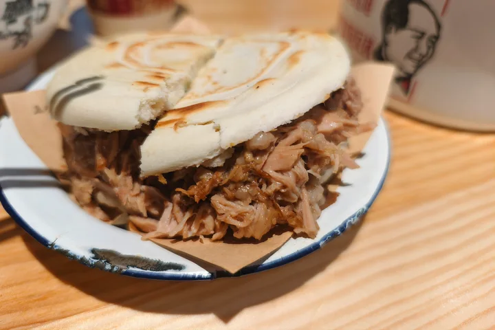 An original photograph of a pork roujiamo with a pale baked flatbread, browned griddle marks and abundant chopped braised pork