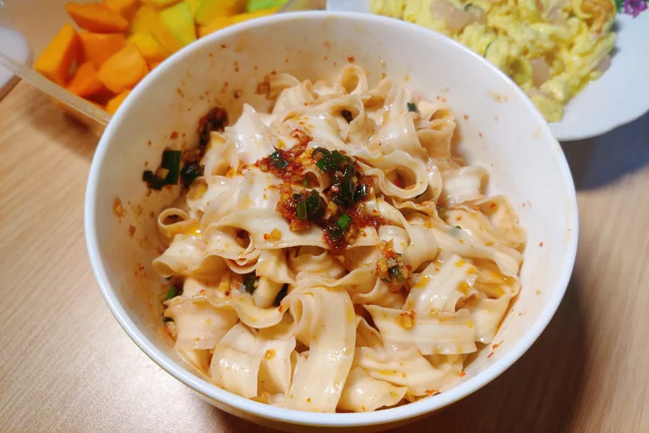A homemade bowl of broad youpo noodles mixed with chilli, garlic and scallion