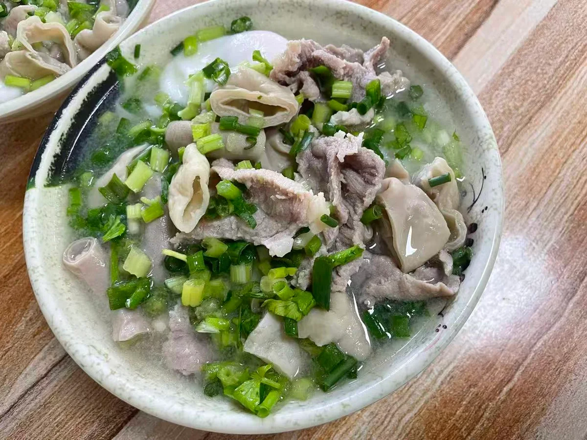 A bowl of Hou'an rice noodles in clear pork broth with sliced pork, pork intestines and chopped scallions